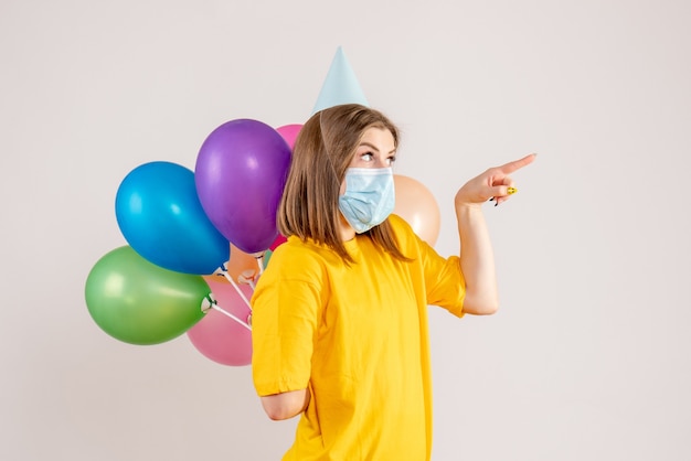 young female hiding colorful balloons behind her back in mask on white