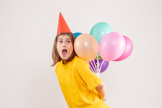 young female hiding colorful balloons on white