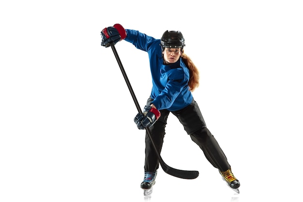 Young female hockey player with the stick on ice court and white wall. Sportswoman wearing equipment and helmet training. Concept of sport, healthy lifestyle, motion, action, human emotions.