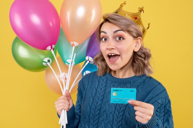 young female holding balloons and bank card on yellow