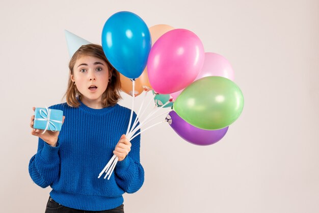 young female holding colorful balloons and little present on white