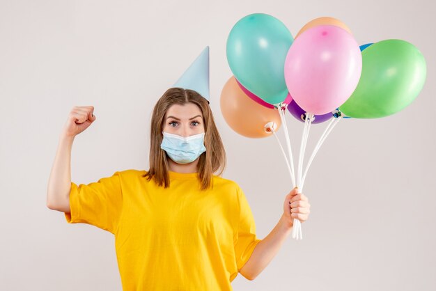 young female holding colorful balloons in mask on white