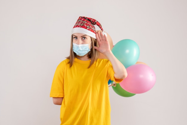 young female holding colorful balloons in mask on white