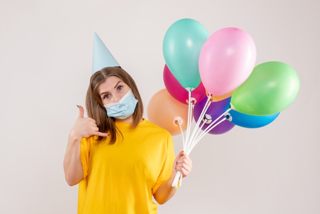 young female holding colorful balloons in mask on white