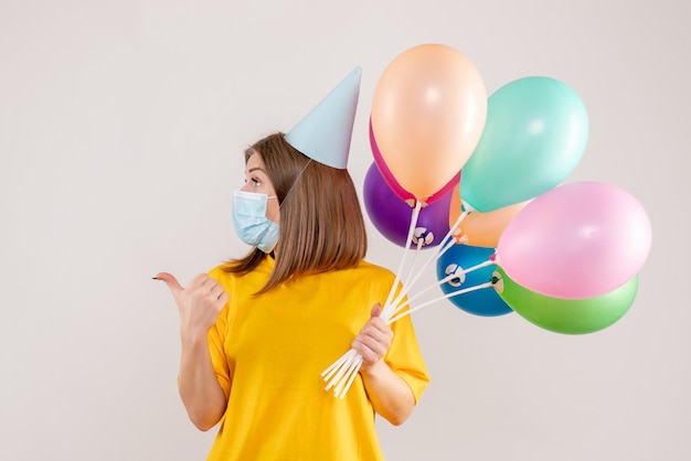 young female holding colorful balloons in mask on white