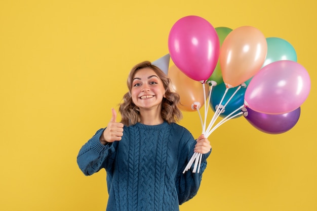 young female holding colorful balloons on yellow