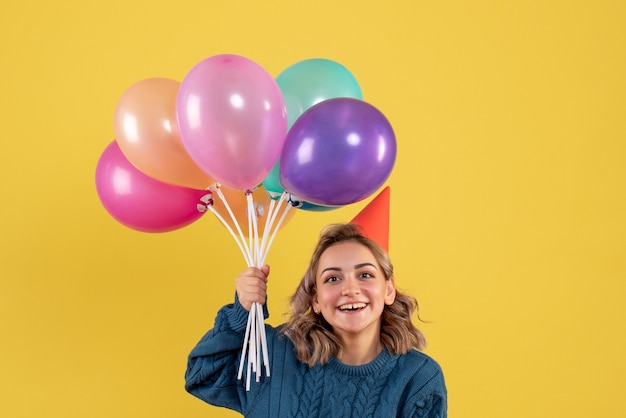 Free photo young female holding colorful balloons on yellow