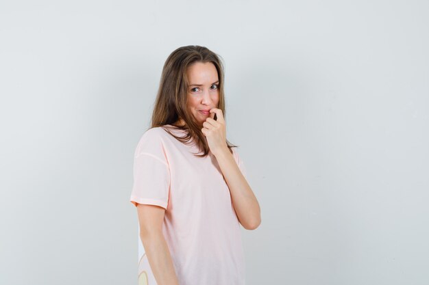 Young female holding finger on her lip in pink t-shirt and looking ashamed. front view.