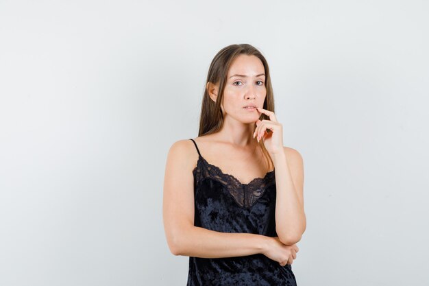 Young female holding finger near mouth in black singlet and looking sensible