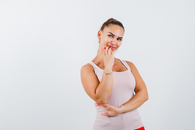 Young female holding hand on chin singlet and looking cute. front view.