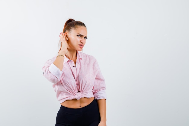 Free Photo young female holding hand behind ear in casual shirt and looking wondered , front view.