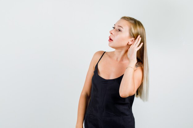 Young female holding hand behind ear to hear in black singlet