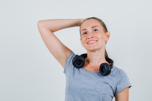 Young female holding hand on head in grey t-shirt and looking dreamy , front view.