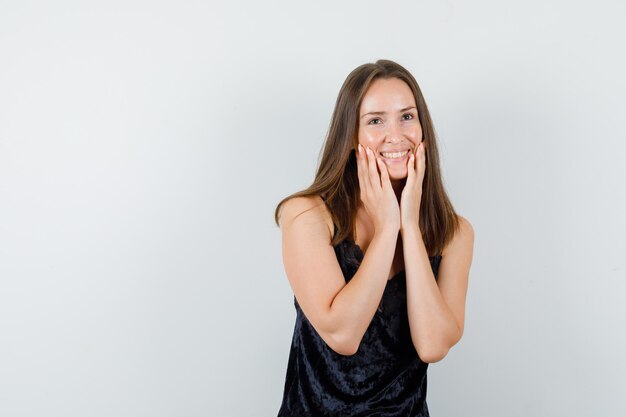 Young female holding hands on cheeks in black singlet and looking joyful.