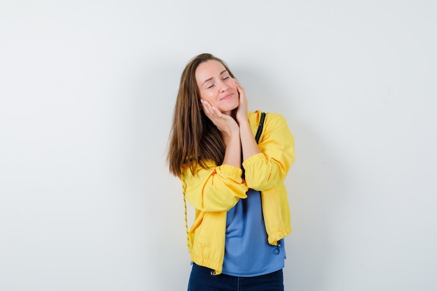 Young female holding hands on cheeks in t-shirt, jacket and looking peaceful. front view.