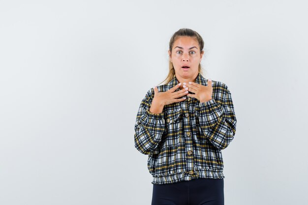 Young female holding hands on chest in shirt, shorts and looking puzzled , front view.