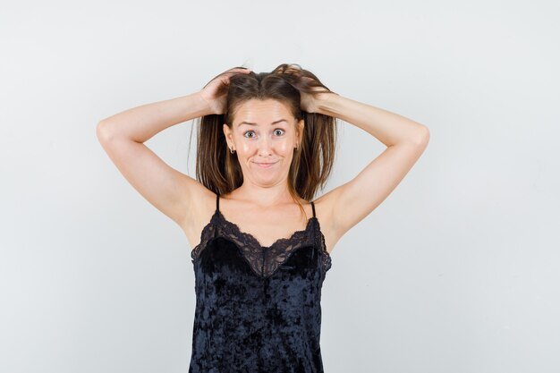 Young female holding hands in hair in black singlet and looking funny