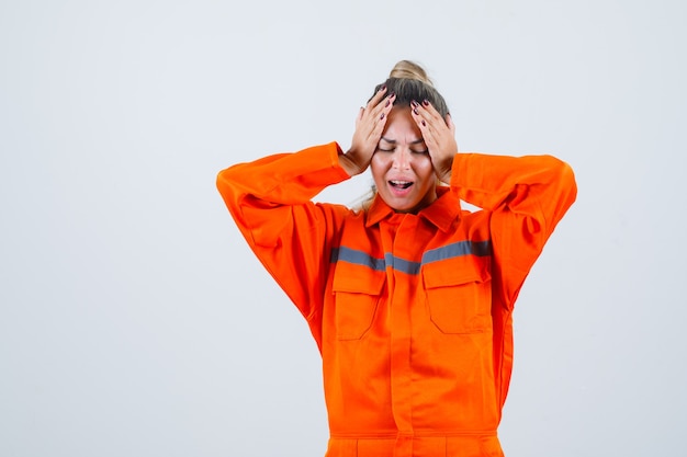 Free Photo young female holding hands on head in worker uniform and looking stressful. front view.