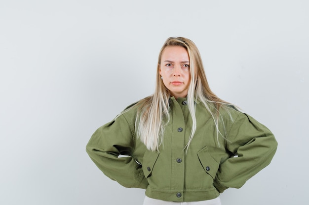 Free photo young female holding hands on her waist in green jacket and looking nervous , front view.