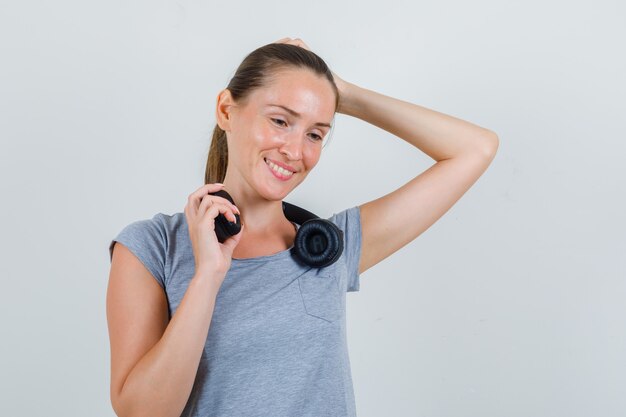 Young female holding headphones in grey t-shirt and looking glad , front view.