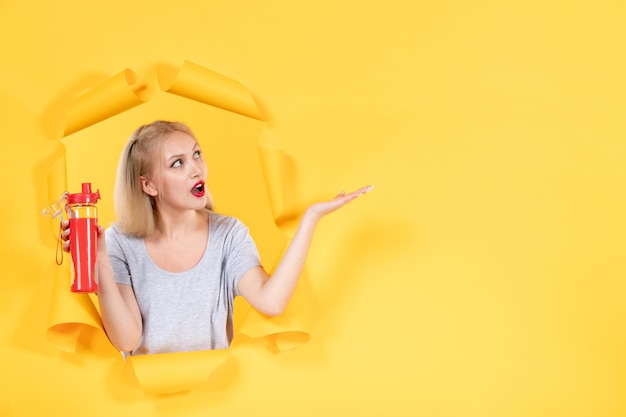 Young female holding red bottle on yellow background gym athlete facial sport