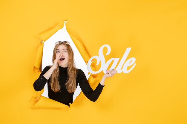 Young female holding sale writing through torn paper hole in the wall