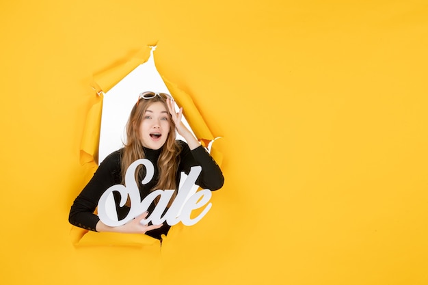 Young female holding sale writing through torn paper hole in the wall