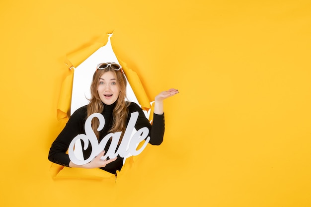 Free photo young female holding sale writing through torn paper hole in the wall