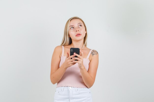 Young female holding smartphone and looking up in singlet, mini skirt .