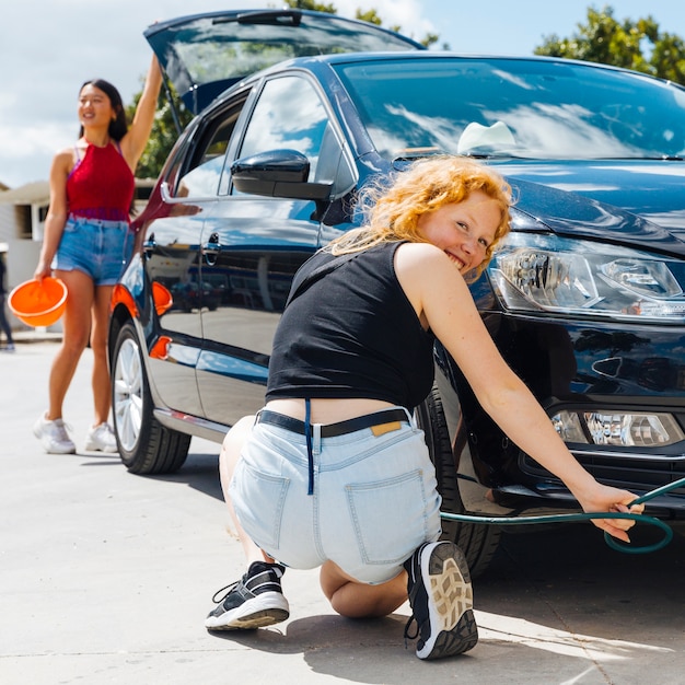 Free photo young female inflating tire of automobile while other woman closing trunk in background