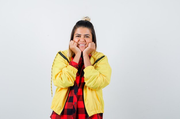 Young female leaning chin on her hands in checkered shirt, jacket  and looking merry. front view.