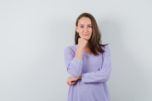 Young female leaning at her fist while smiling at camera in lilac blouse and looking fresh 