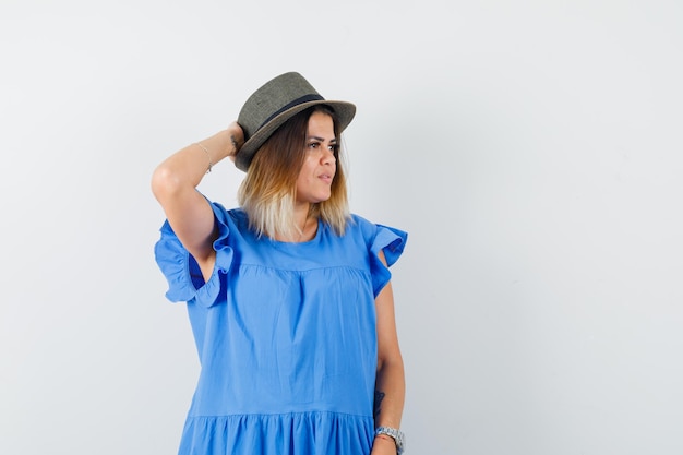 Free photo young female looking aside with hand behind head in blue dress, hat and looking delightful