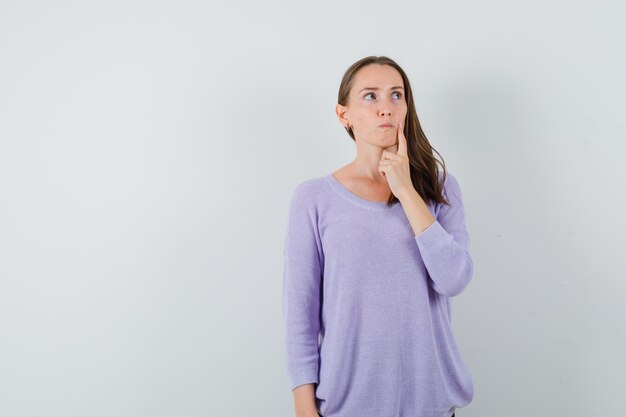 Young female looking away in lilac blouse and looking thoughtful. front view.