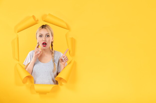 Young female looking from torn yellow paper background facial window indoors sale