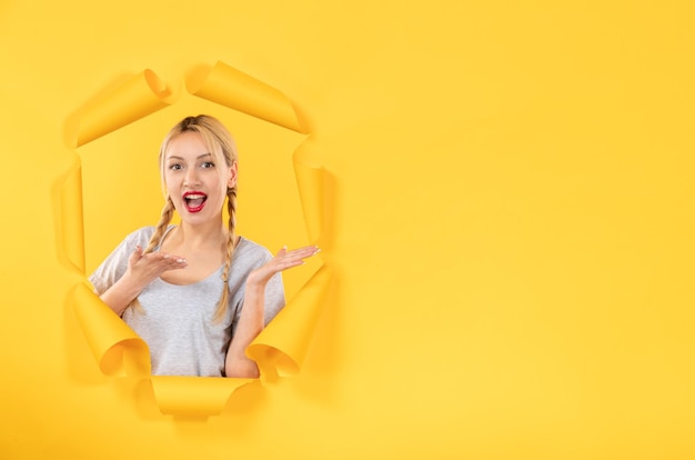 Young female looking from torn yellow paper surface facial window indoor sale