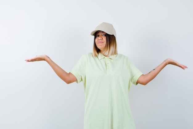 Free Photo young female making scales gesture in t-shirt, cap and looking confident. front view.