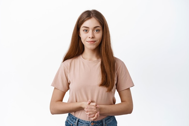 Free photo young female model standing ready at your service holding hands together near chest wanting to help smiling and looking determined standing over white background