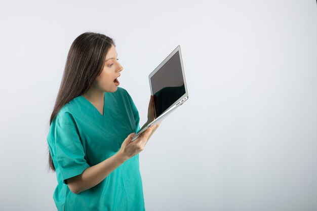 Young female nurse looking at laptop on white. 