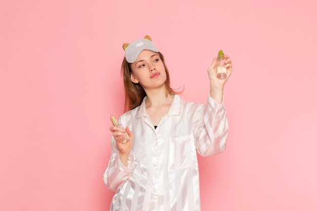 young female in pajamas and sleep mask posing holding spray on pink