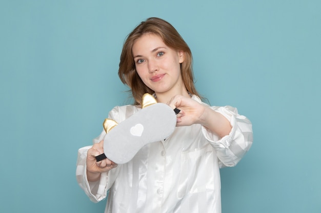 Free photo young female in pajamas and sleep mask smiling and posing on blue