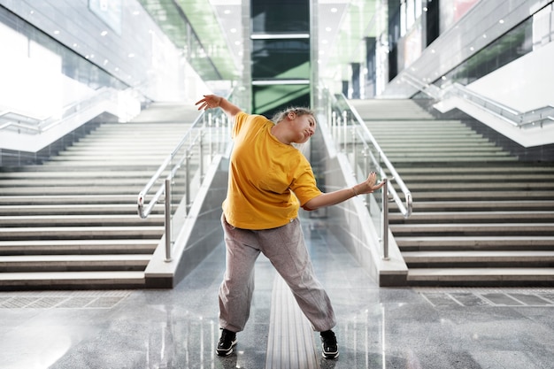 Free photo young female performer dancing next to stairs indoors