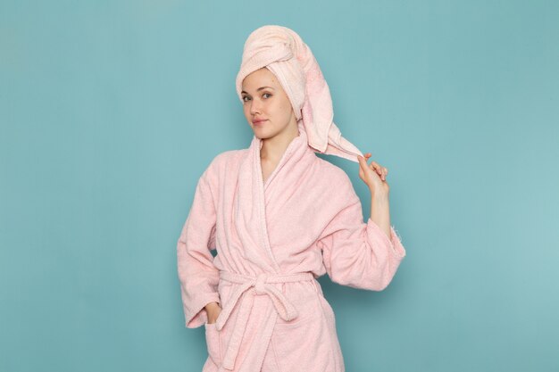 young female in pink bathrobe after shower posing smiling on blue