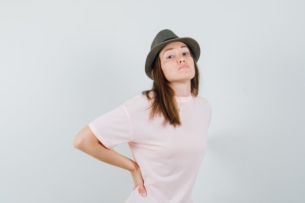 Young female in pink t-shirt, hat suffering from backache and looking tired , front view.