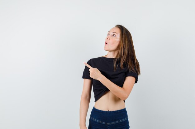 Young female pointing away while looking up in black blouse