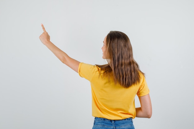 Free Photo young female pointing finger up and smiling in t-shirt, shorts , back view.