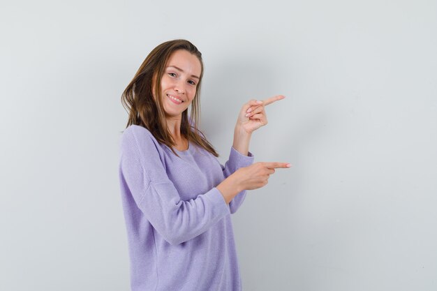 Young female pointing to left side in lilac blouse and looking satisfied. front view.