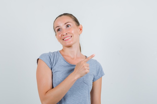 Young female pointing to side in grey t-shirt and looking cheery. front view.