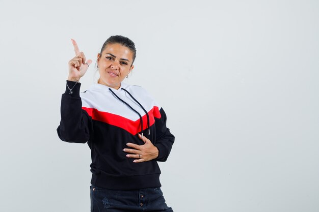 Young female pointing up in colorful sweatshirt and looking assured , front view. 