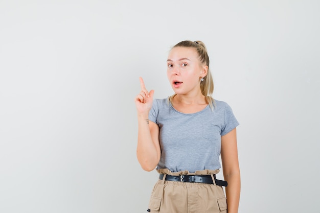 Young female pointing up, having excellent idea in t-shirt, pants , front view.